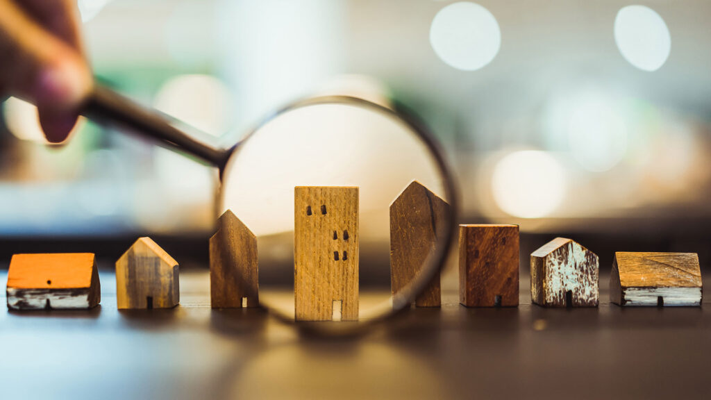 Hand holding magnifying glass looking at wooden houses