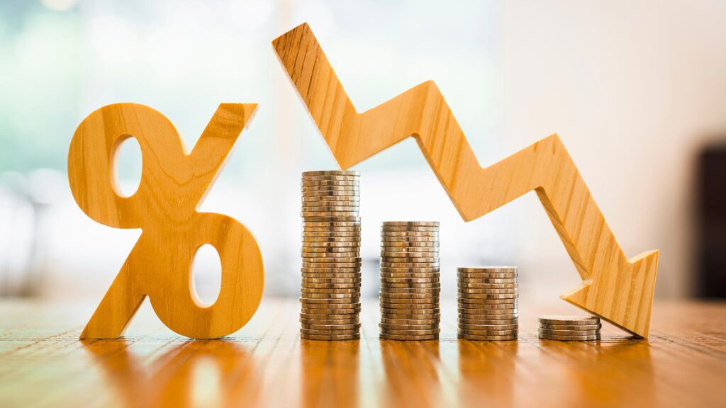 Wooden percentage sign with downward arrow and decreasing stacks of coins